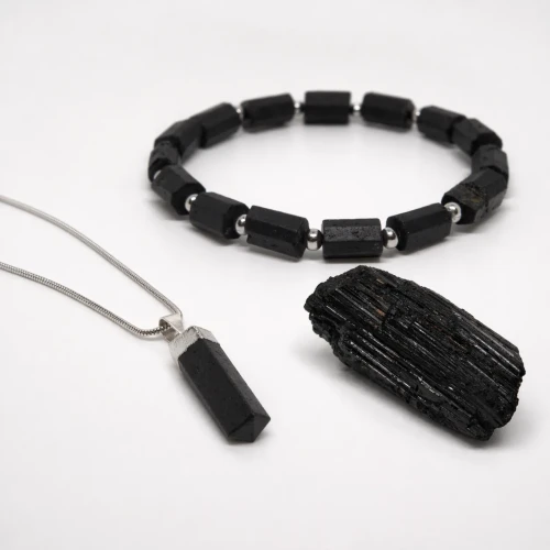 Zestaw ochronny z czarnego turmalinu – zbliżenie na naszyjnik z grotem, bransoletkę i surowy kamień.