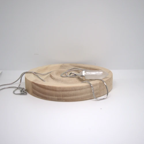 Naszyjnik z Kryształu Górskiego na drewnianej podstawce, subtelna biżuteria energetyczna z jasnym kamieniem w formie grotu.