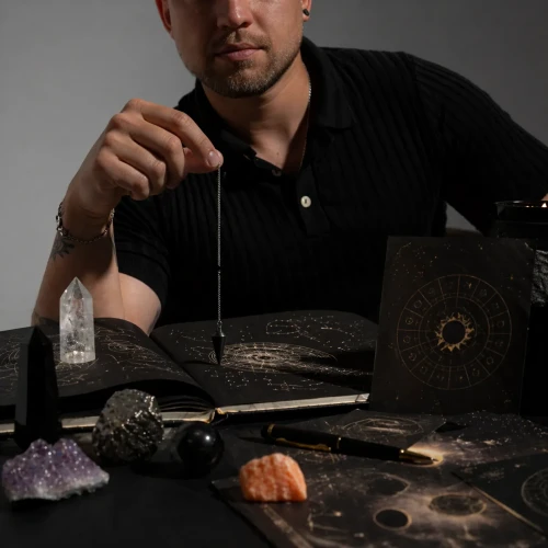 Damian podczas osobistej odpowiedzi astrologicznej z wahadłem, kryształami i symboliką zodiaku przy klimatycznym stole do pracy energetycznej.