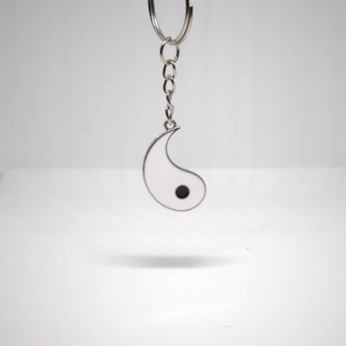 Biały breloczek Yin Yang zawieszony na kółku, stal nierdzewna, minimalistyczny symbol równowagi.