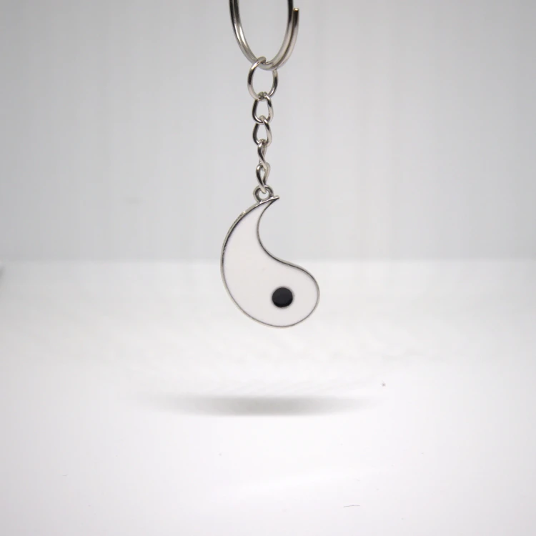 Biały breloczek Yin Yang zawieszony na kółku, stal nierdzewna, minimalistyczny symbol równowagi.