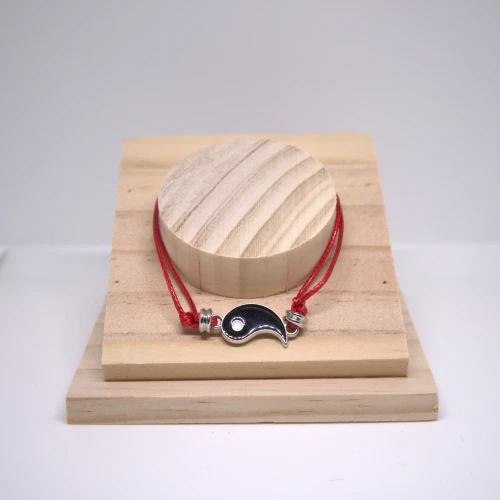 Czarna bransoletka Yin Yang na czerwonej nitce, stal nierdzewna, minimalistyczna biżuteria intencyjna na drewnianej podstawce.